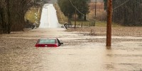 a partially submerged car in flood waters in the middle of a street