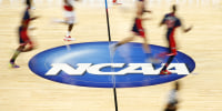 Players dribble the ball on the NCAA logo at half court