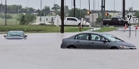 Two cars are caught in flood waters on a street outside