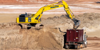 An excavator pours Uranium tailings into a container truck