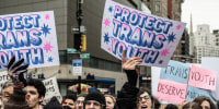 Demonstrators hold signs that read, "Protest Trans Youth."