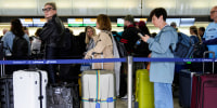 People wait in line with their luggage at an airport