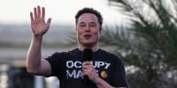 Elon Musk raises his hand while he speaks,