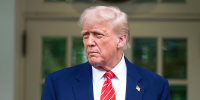 Donald Trump stands outside behind a shrub as a marine in the background salutes him