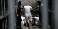 Prisoner led by two security officers inside a cell.