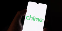 A hand holding a cellphone with the Chime logo on the screen.