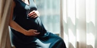 Pregnant Woman Touching Her Belly While Sitting On Window Ledge