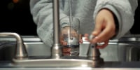 Person holding clear glass container under a sink.