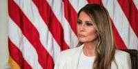 Melania Trump seated in front of an American flag backdrop