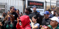 People gather in front of Ambiance Apparel after several employees were taken into custody by federal agents