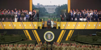 Image: A grandstand with attendees, including Trump and Melania, with soldiers and army tanks below it.