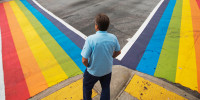 A pedestrian waits to cross a rainbow painted crosswalk