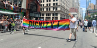 People march with a rainbow sign that says "Dignity"
