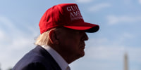 Donald Trump side profile, his face covered in shadow, wearing a red cap