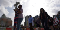 A woman holds a cross as she protests with others.