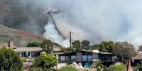 A firefighting helicopter works to extinguish the Rancho Fire as smoke rises at Laguna Beach