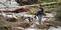 A person cover their face with their hand while standing in flood debris and fallen trees