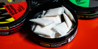Wip containers displayed on a red table, one of the containers is open and shows white pouches filled with powder inside