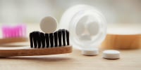 Side view of white toothpaste tablets with fluoride. Dental care concept. Natural ingredients, side view of bamboo toothbrush with white toothpaste tablet on brushes, blurred jar on background.