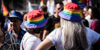 Two people wear rainbow bucket hats in a crowd outside