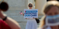 A demonstrator holds a sign that reads, "Moving Forward, Protecting Our Care"