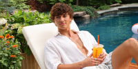Gavin Casalegno sits in a pool chair by the pool holding a Dunkin Donuts Golden Hour refresher drink