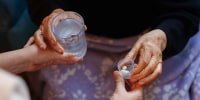 An elderly woman taking a glass of water and pills.