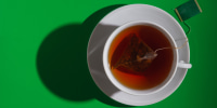 Tea in a white cup and saucer is brewed from a pyramid-shaped bag