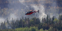 Aerial view of helicopters putting out fires over trees, smoke in the air
