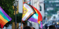 An LGBTQIA flag is waved above a crowd