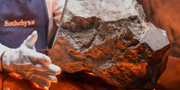 A gloved hand hovers near a rock on a table top