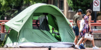People walk past tents at a homeless encampment