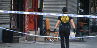 A cop walks through a crime scene on a sidewalk with police tape draped across