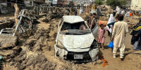 People gather near a damaged vehicle and scattered debris after  a flood