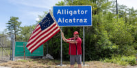 A man wearing a "Make America Great Again" hat waves a flag outside the detention center called "Alligator Alcatraz" near Ochopee, Fla., on July 12 , 2025. 