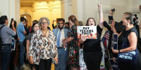 Senfronia Thompson, left, walks past a crowd of people into the House Chamber, a person holds a sign that says "put Texans first"
