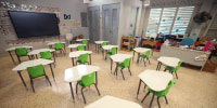 A classroom with desks, a large screen on the left wall, two fans can be seen