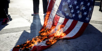 An American flag burns on the ground