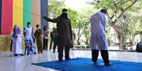 An official uses a rattan cane to whip a man convicted of violating Islamic law by hugging and kissing 