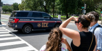 An Immigration and Customs Enforcement police SUV patrols on the road as people watch from the sidewalk