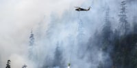 A helicopter drops water on a hotspot on the fire's edge on Aug. 6, 2025.