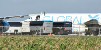 People board a plane outside in front of four charter buses