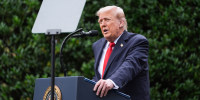 Donald Trump speaks at a podium with a bullet proof glass pane in front of him