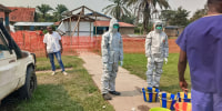 Men in hazmat suits stand outside