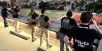 Officers stand on the roof of a building and watch a high school football game