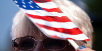 An attendee uses a handheld fan for shade during a naturalization ceremony.