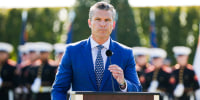 Secretary Pete Hegseth stands at a podium to speak to US troops who stand behind him. 