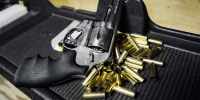 A Smith & Wesson .357 magnum revolver next to spent bullets on a black tray