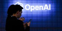 Visitors look at their phone next to an Open AI logo on a blue tiled wall