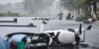 a fallen motorbike on the street outside during a storm, people ride on motorbikes in the distance